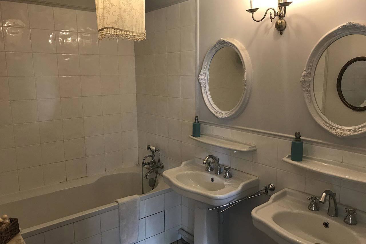Un baño con dos lavamanos, una bañera y dos espejos fijados a la pared.