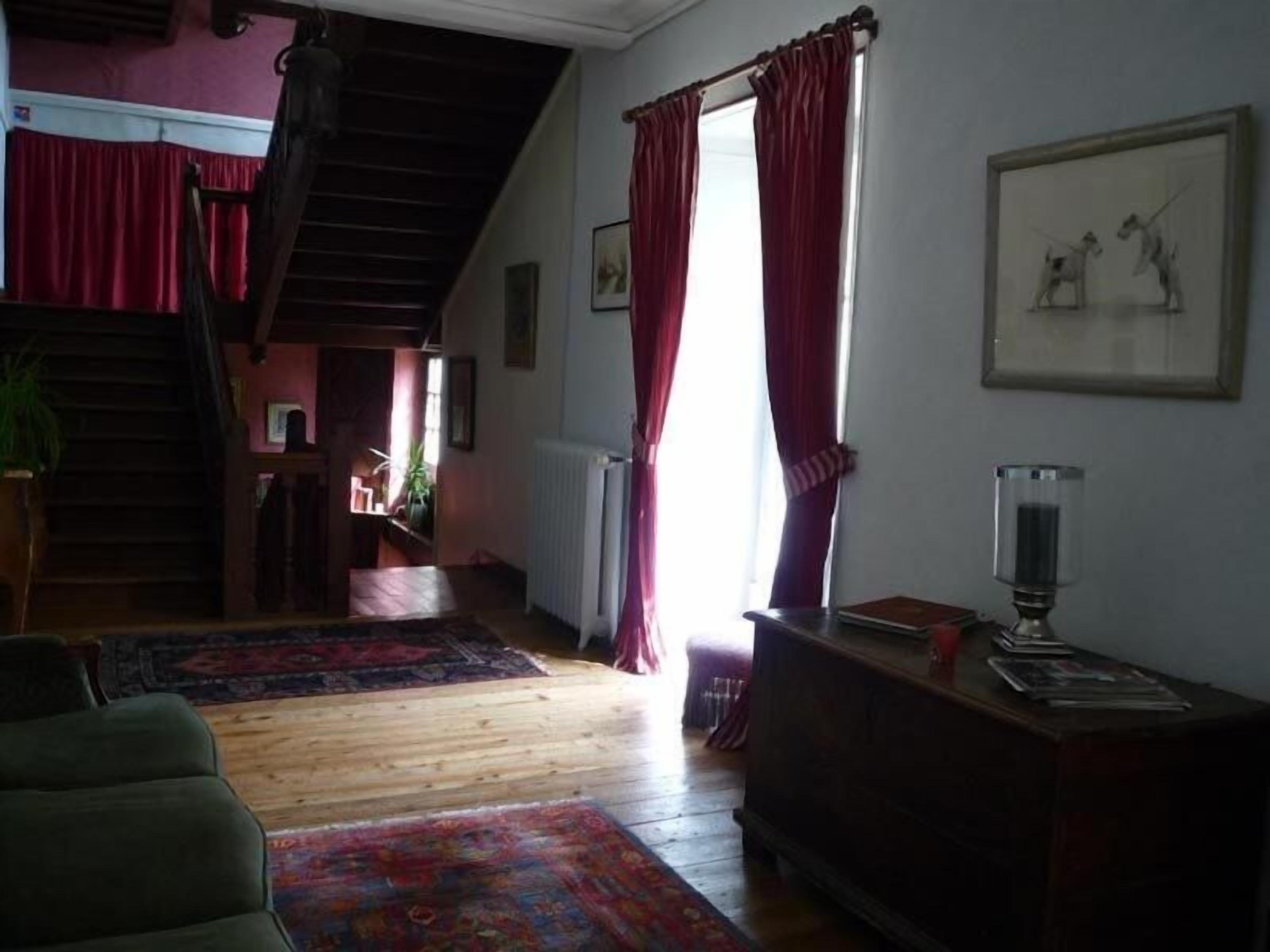 A cozy living room with a staircase, wooden floors, and red curtains.