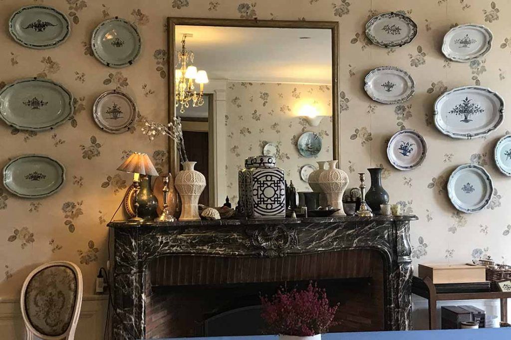 Une pièce avec une cheminée en marbre, un miroir et divers objets décoratifs accrochés au mur.