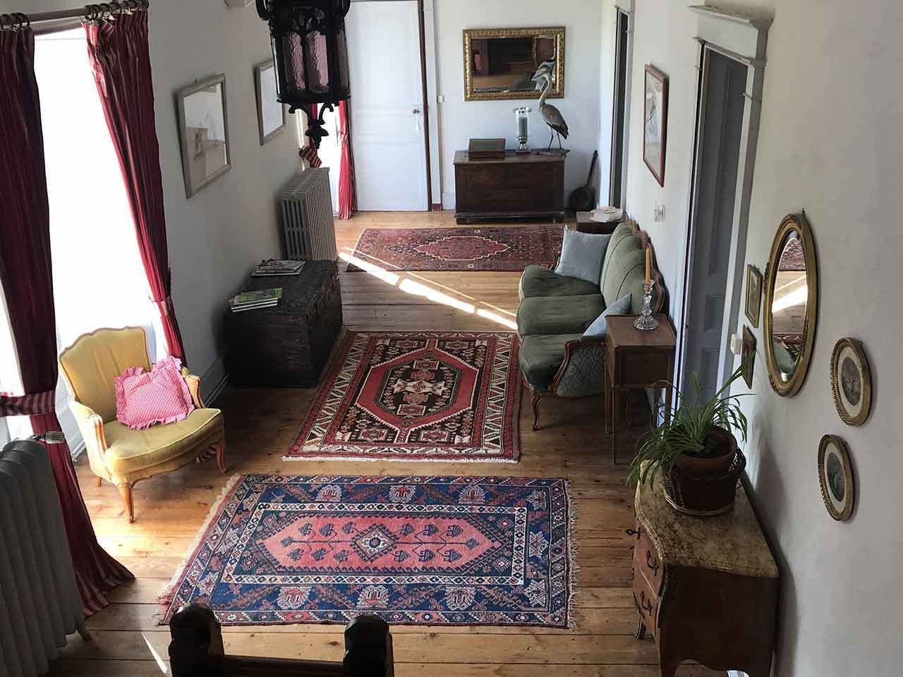 Un salón amplio con piso de madera, un sillón verde, un sillón amarillo y un tapete rojo y azul con estampado.