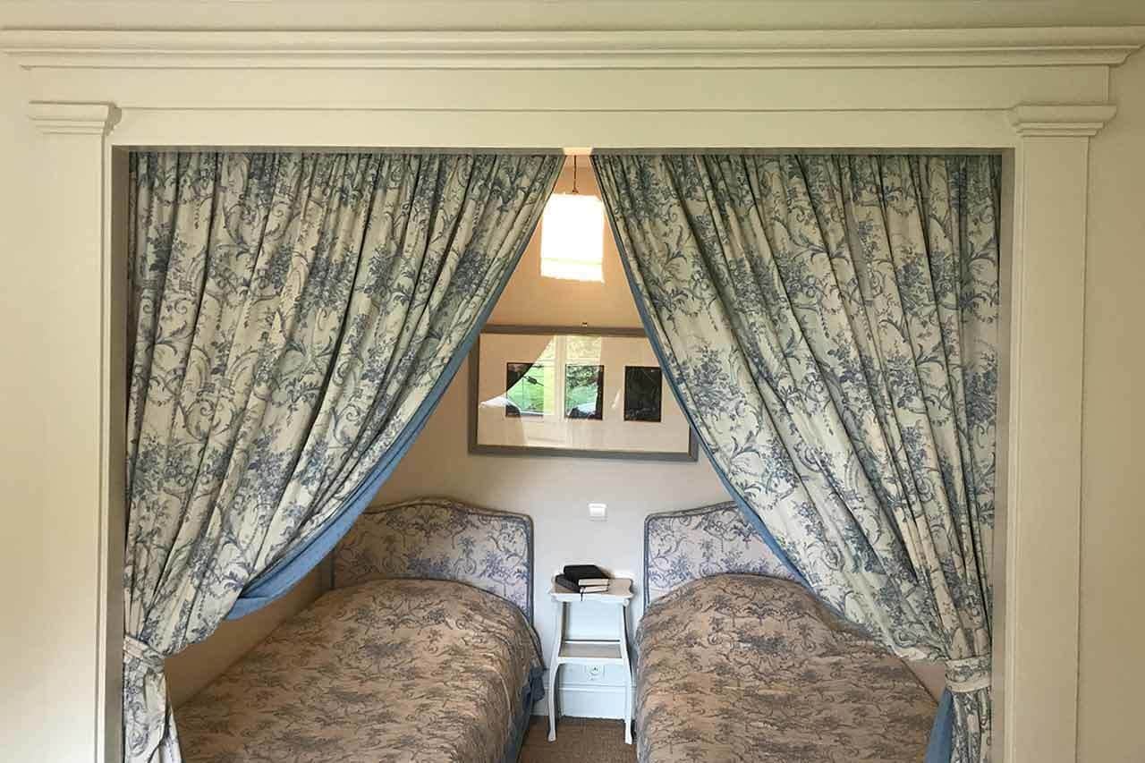 A bedroom with two beds, a small table, and a window with curtains.