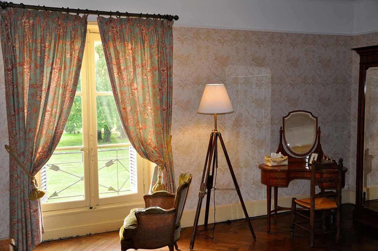 Una habitación con un ventanal grande, una lámpara de pie, un espejo y una silla de mimbre.