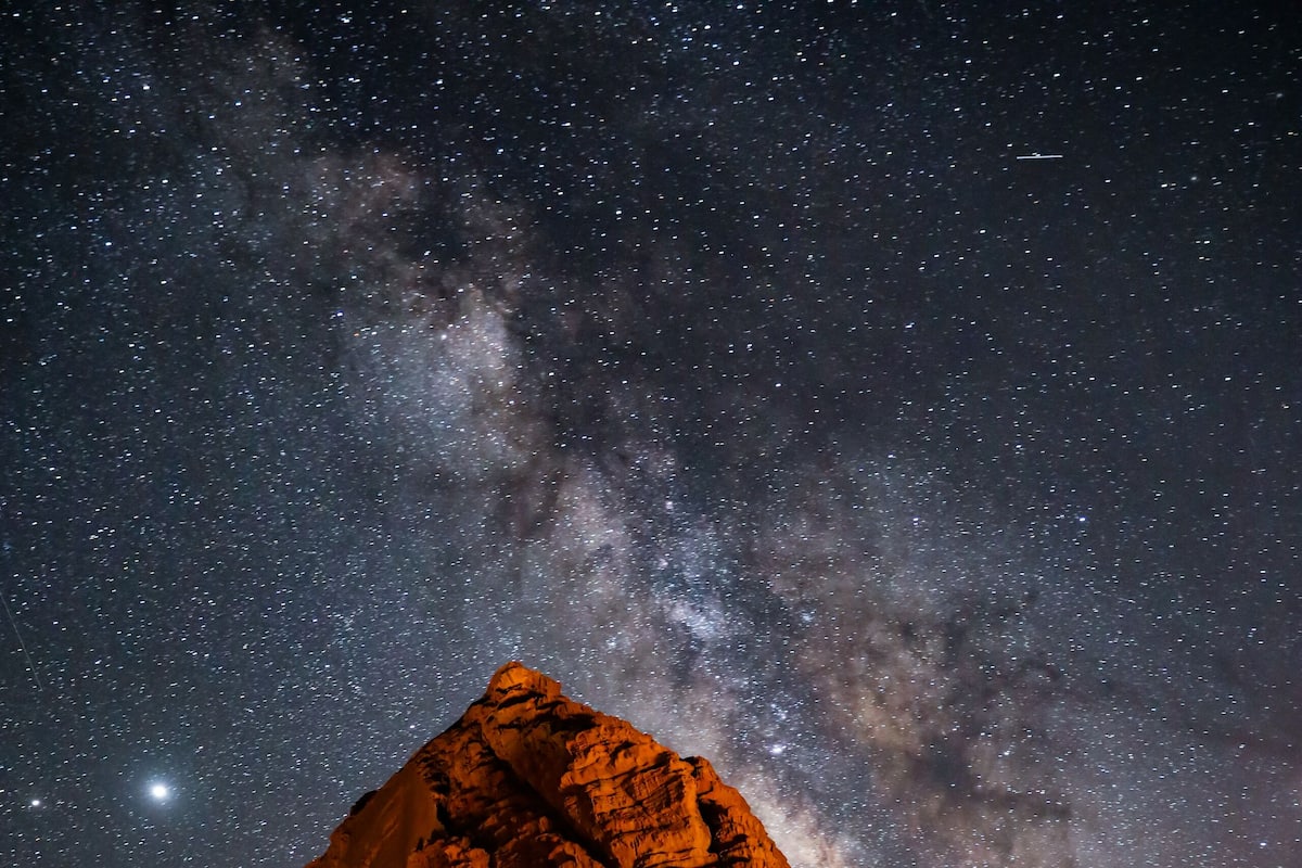 A tent set up against a rocky mountain under a starry night sky with the Milky Way visible.
