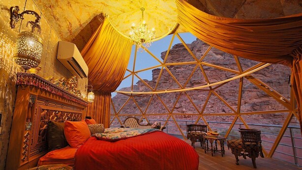Ein Zimmer mit einem Bett, einer Kandelaber und Blick auf felsiges Gelände durch ein großes Fenster.