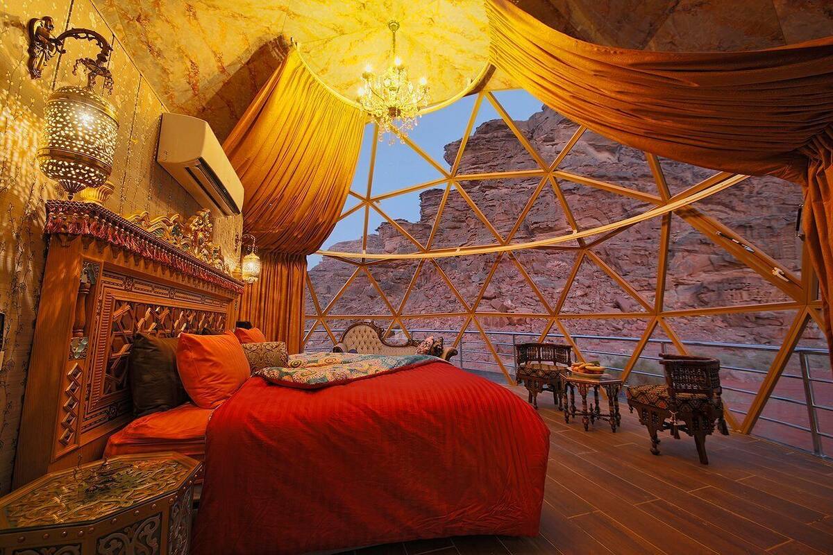 A room with a bed, a chandelier, and a view of rocky terrain through a large window.