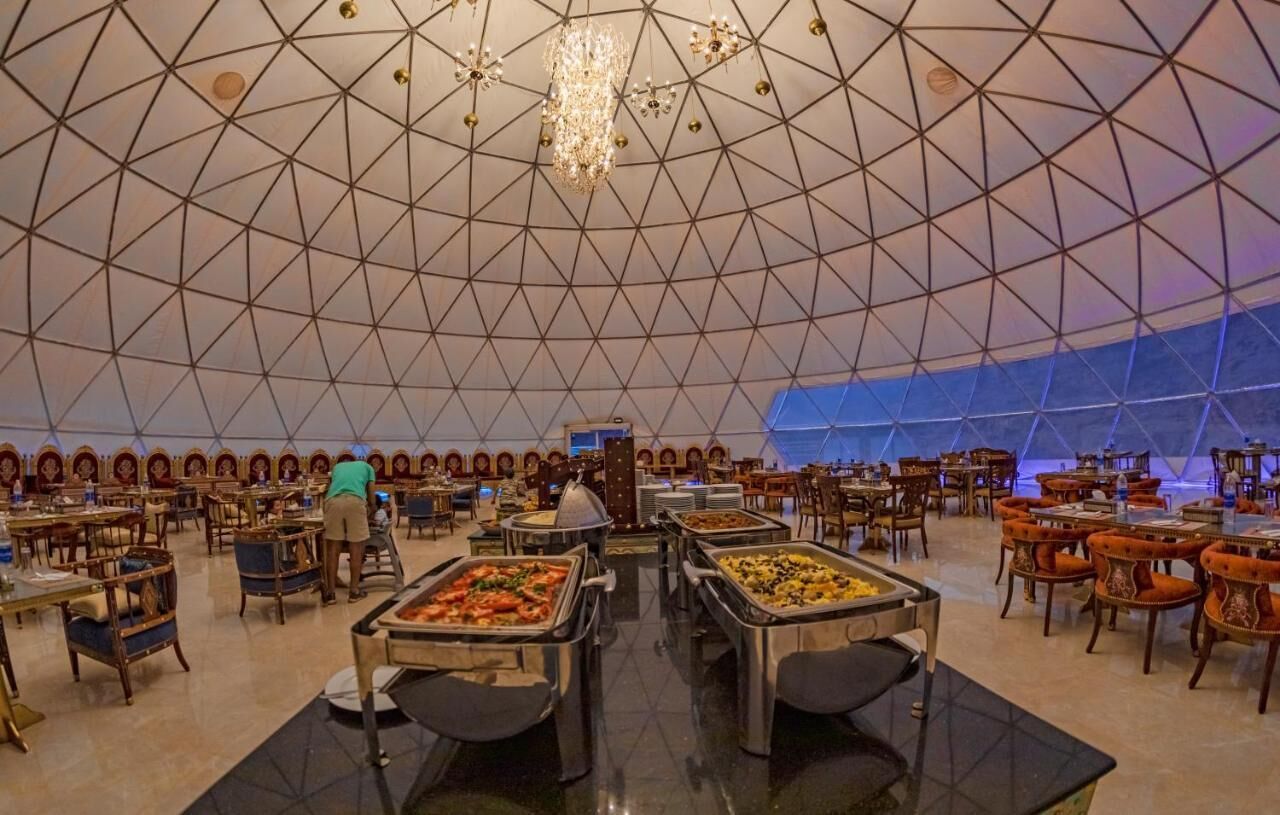 Una gran sala de dinar amb un disseny geomètric al sostre, diverses zones de menjar a la planxa i un llum central.