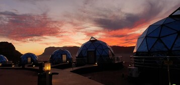 Geodesic dome structures with a walkway leading to them, set against a sunset sky.