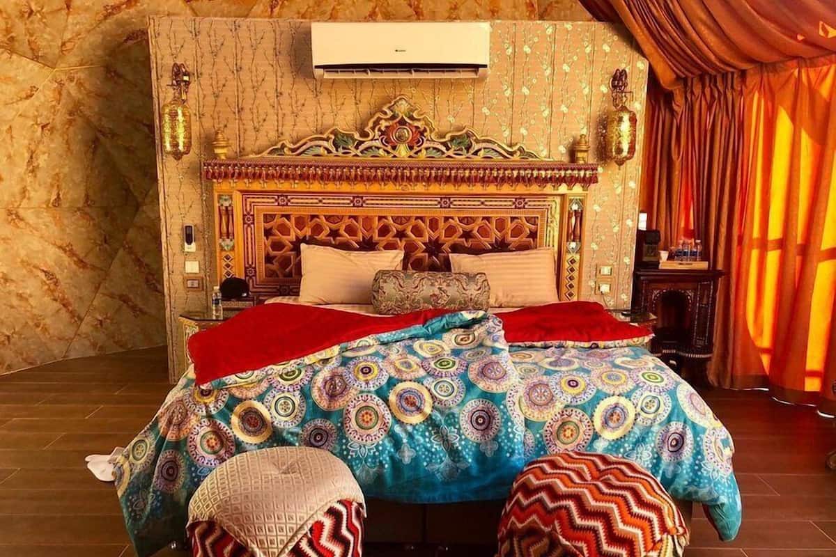 A room with a patterned bedspread, a decorative headboard, and a red curtain.