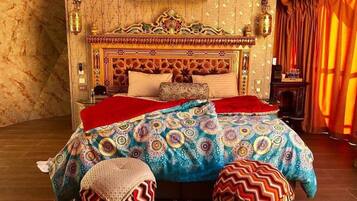 A room with a patterned bedspread, a decorative headboard, and a red curtain.