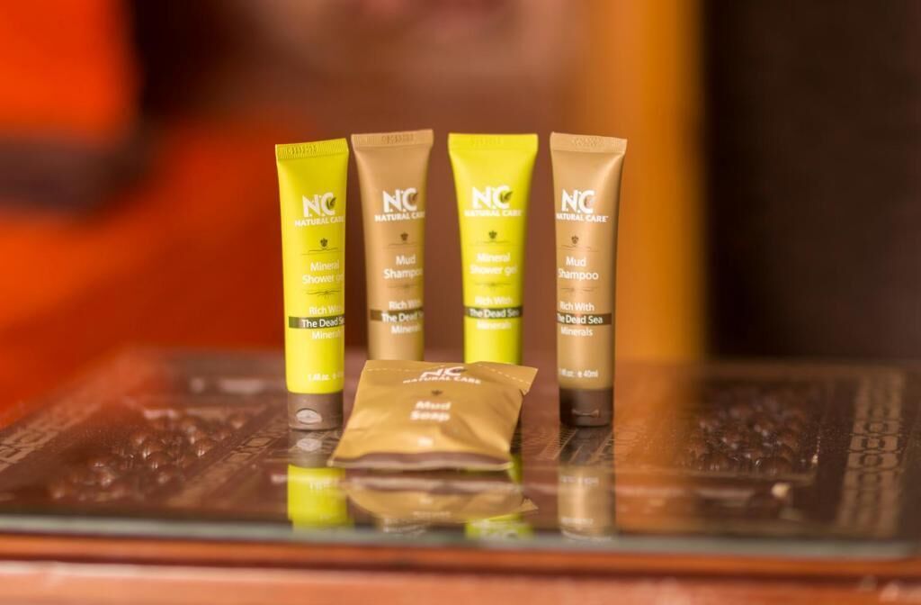 Four tubes of Natural Care products and a packet of body scrub on a reflective surface.