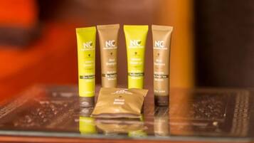 Four tubes of Natural Care products and a packet of body scrub on a reflective surface.