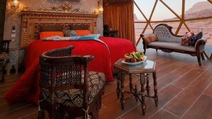 Ein luxuriöses Schlafzimmer mit einem großen Bett, einer Chandelieber, einer Couch und Blick auf die Berge.
