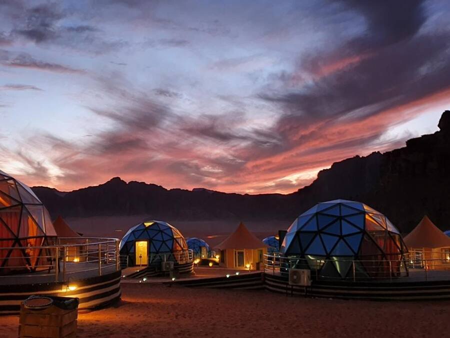 A series of geodesic dome structures with a flat roof, arranged in a semi-circle on a flat terrain, under a twilight sky.