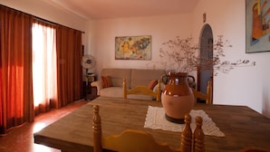 A living room with a wooden table, a sofa, a vase with branches, and a painting on the wall.