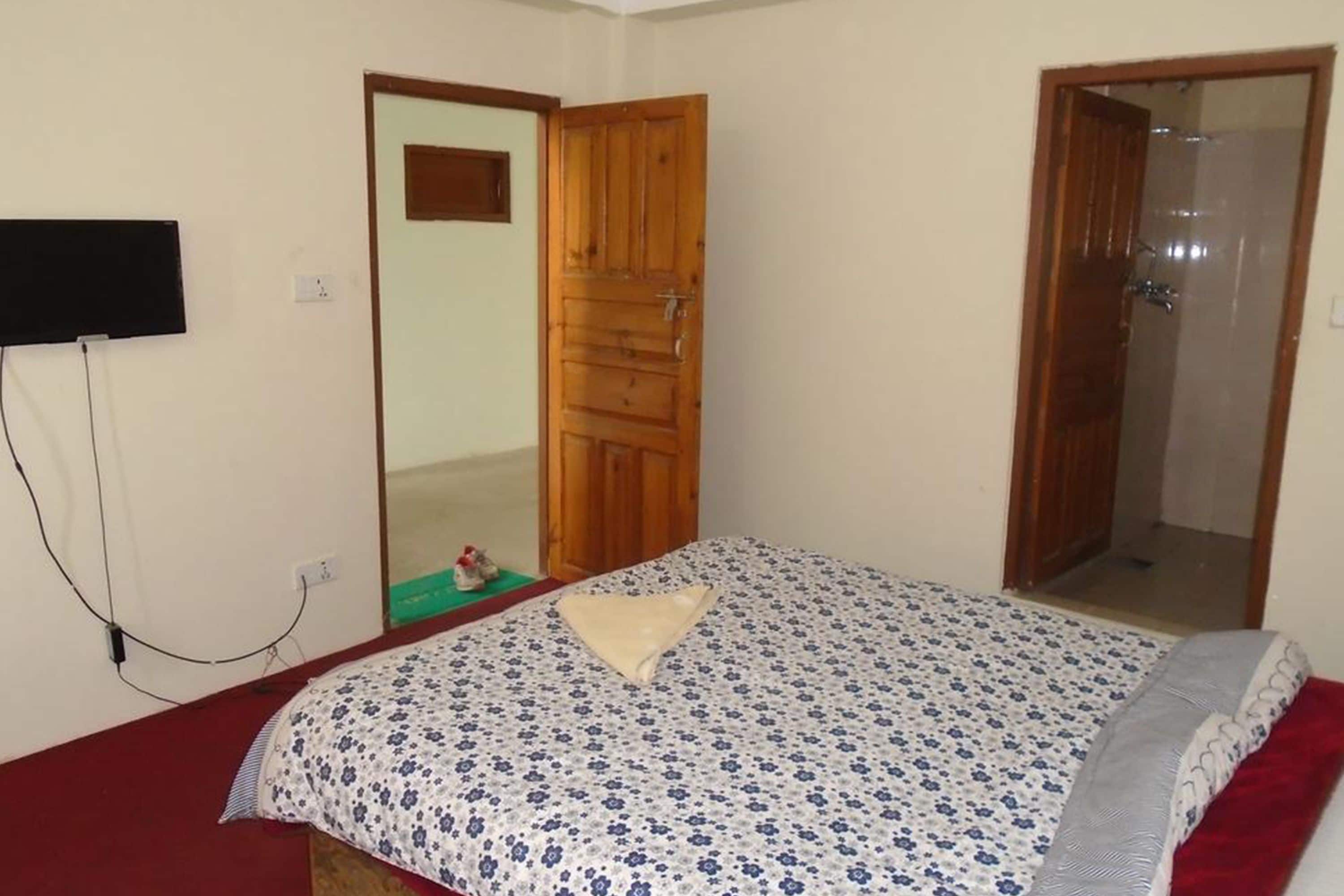 A bedroom with a bed, a wooden door, a mirror, and a TV mounted on the wall.