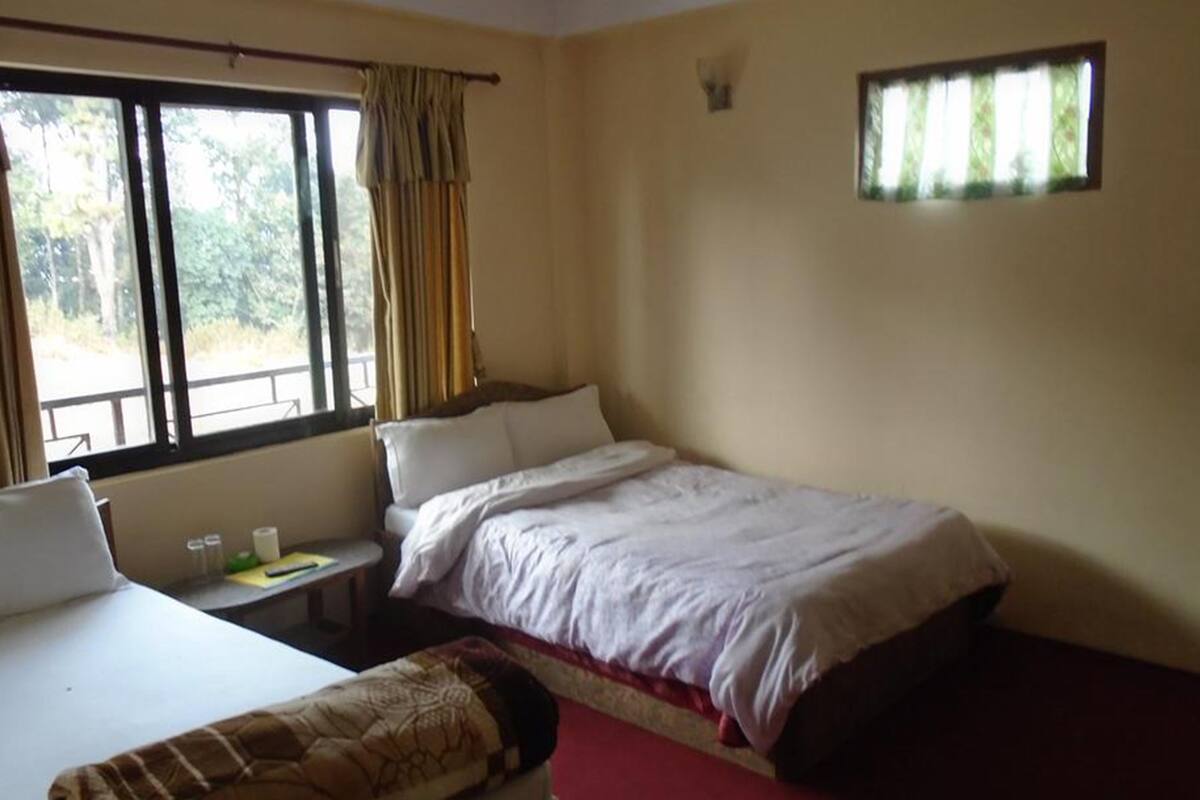Un dormitorio con cama, mesita de noche, silla y ventana con cortinas.