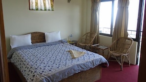 A hotel room with a bed, two wicker chairs, a small table, and a window with curtains.