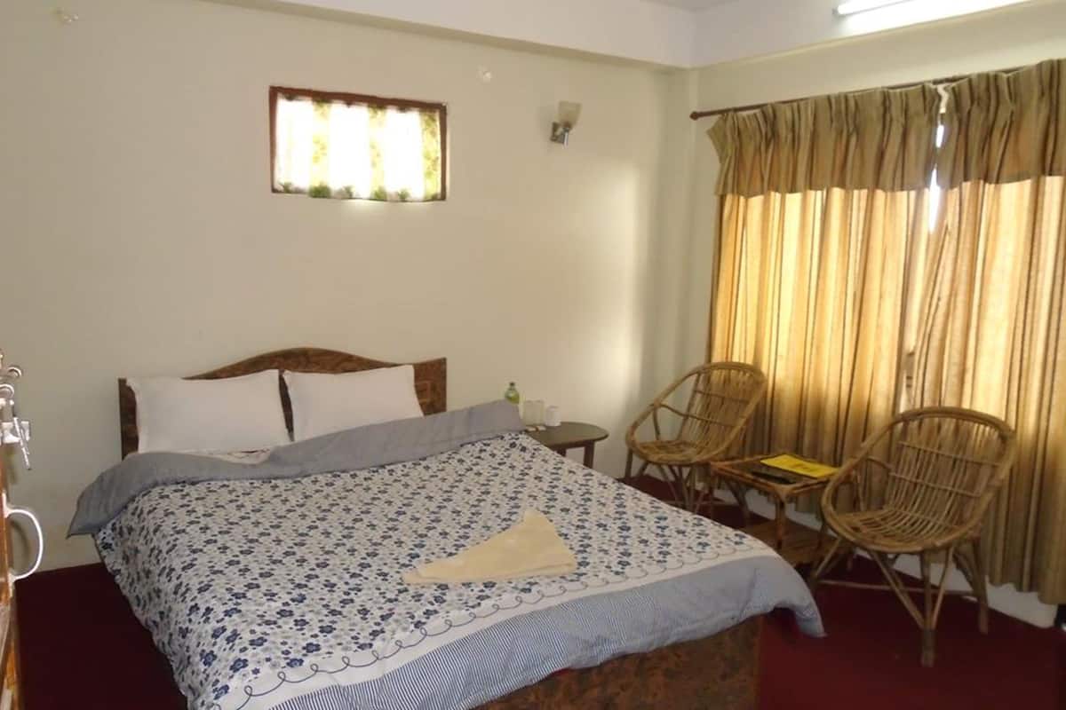 Habitación de hotel con una cama, dos sillas, una mesita y una ventana con cortinas.