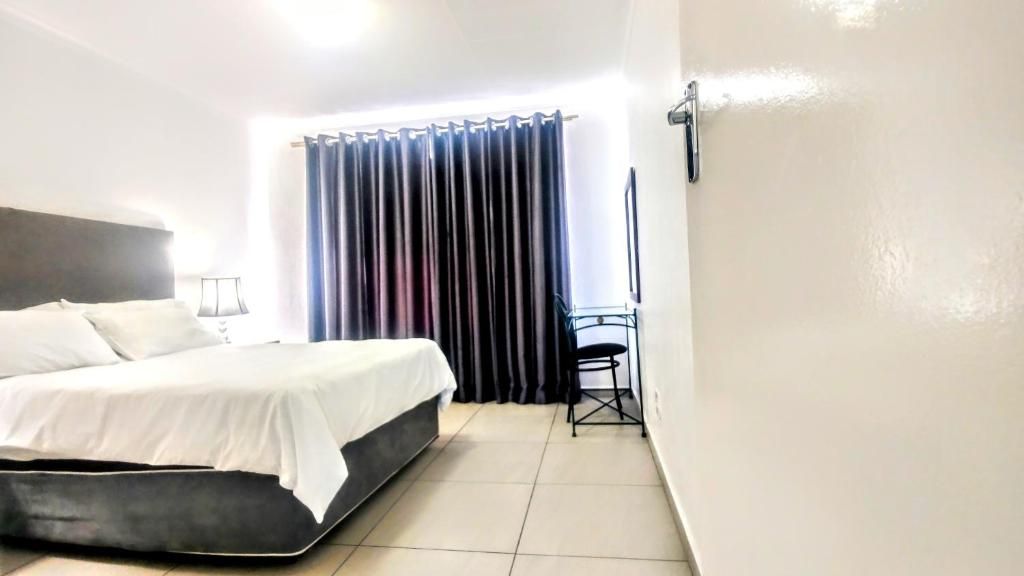 A hotel room with a bed, a chair, a desk, and a window with curtains.
