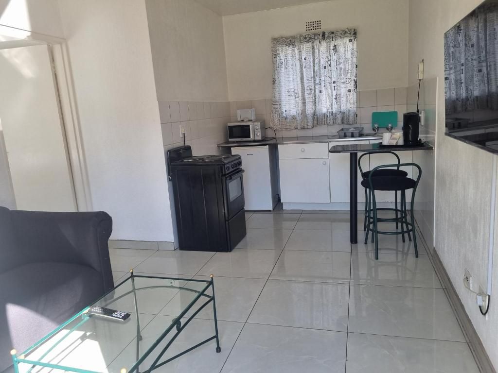 Un espacio habitable compacto con kitchenette, una mesa de centro de vidrio, un sofá negro y un área de comedor con dos sillas.