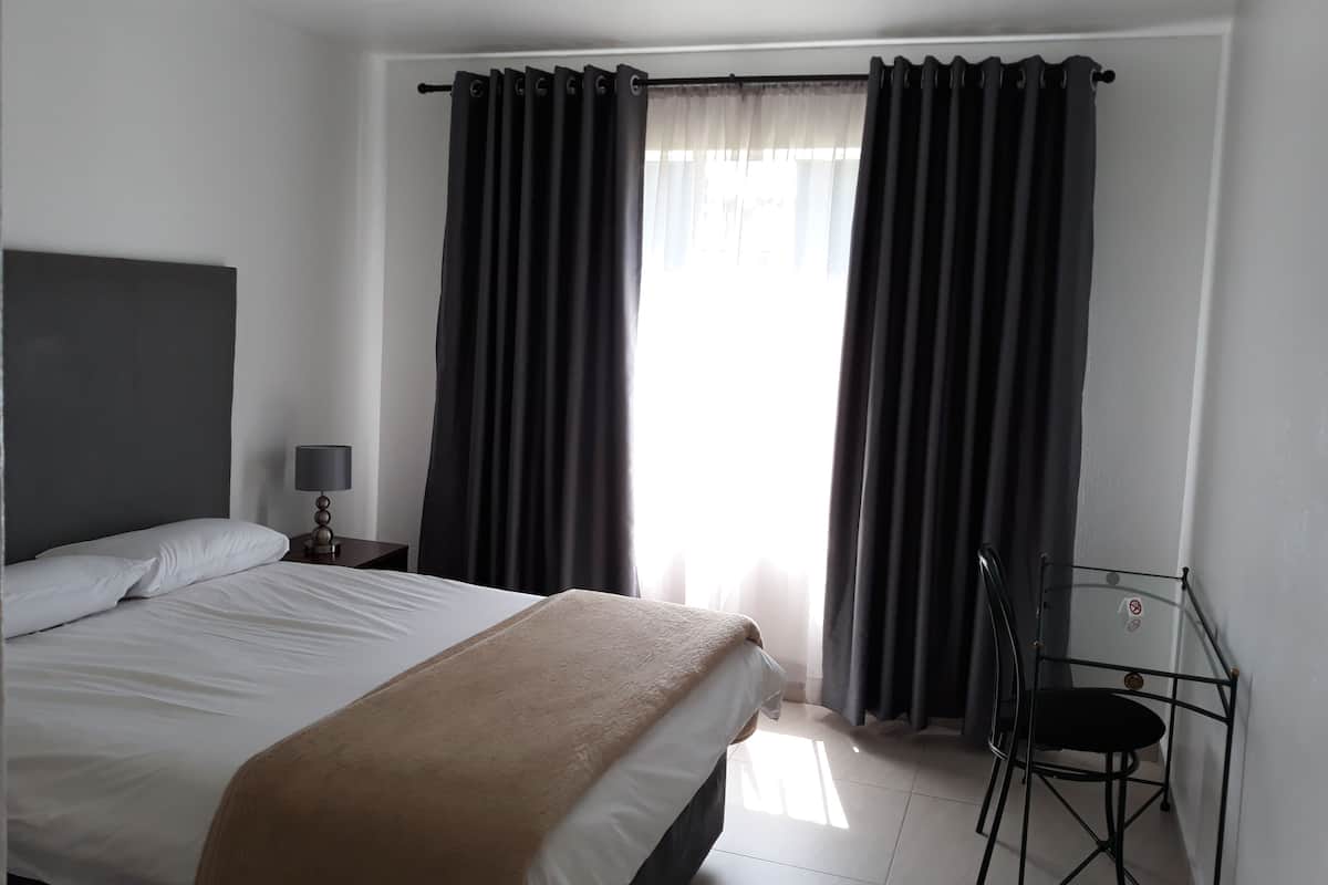 A hotel room with a bed, a bedside lamp, a chair, and a window with curtains.