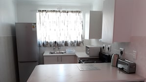 Eine kleine Küche mit Kühlschrank, Mikrowelle, Toaster und Spüle. In der Mitte stehen zwei Stühle und ein Tisch.