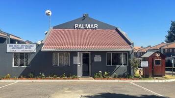 A small building with a sign that reads 'PALMAR' and another sign stating 'THE MOST AFFORDABLE APARTMENT HOTEL DAILY - MONTHLY'.