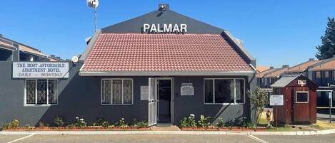Un pequeño edificio con un letrero que dice 'PALMAR' y otro letrero que indica 'HOTEL APARTAMENTOS MÁS ECONÓMICO, DIARIO - MENSUAL'.