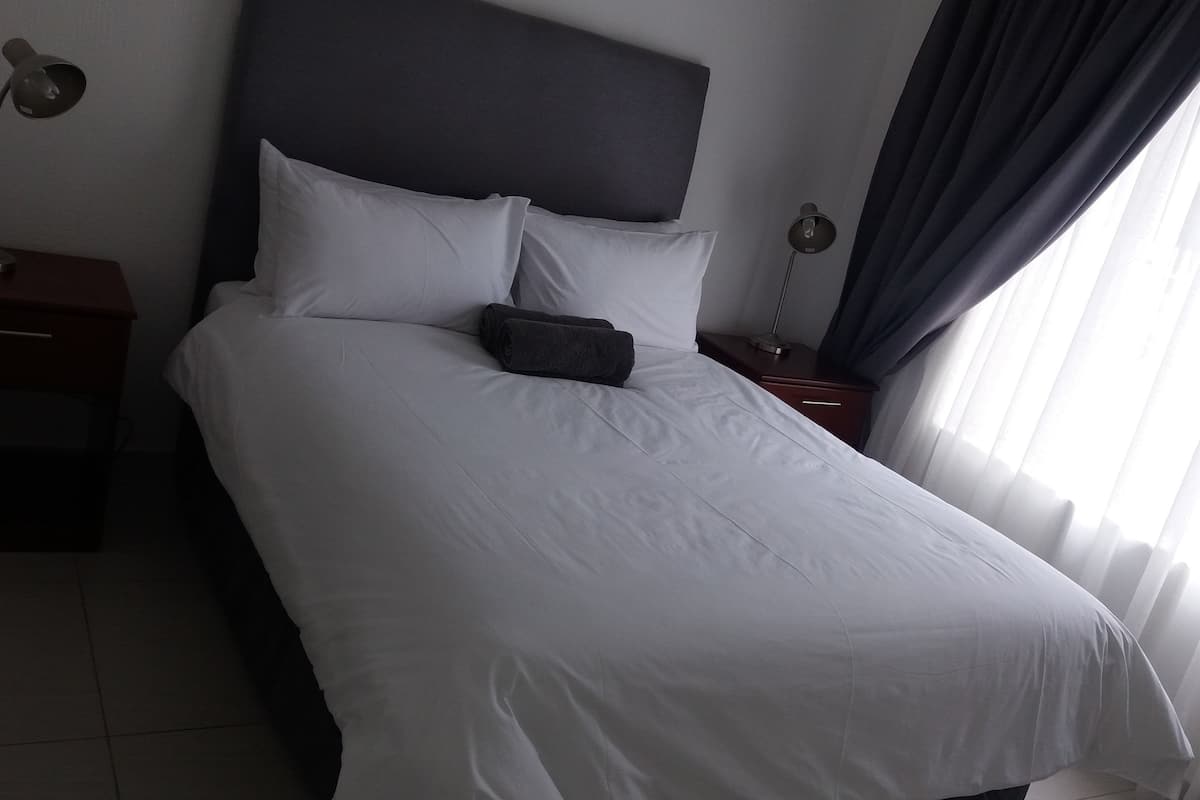 A neatly made bed with white linens, a dark headboard, and a small bedside table with a lamp.