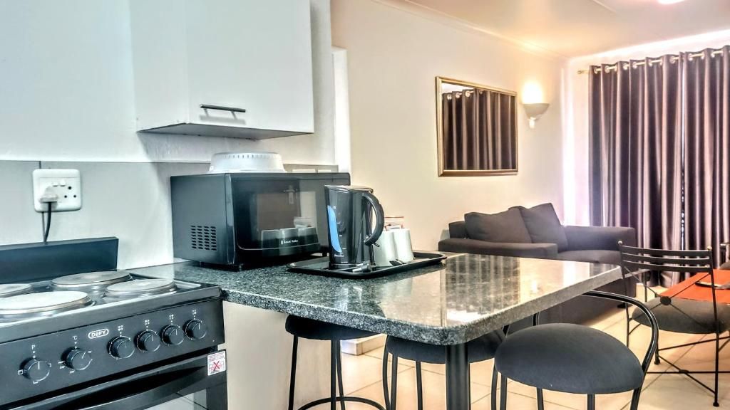 Cocina compacta con estufa a gas, microondas y cafetera. En la zona de estar, hay un taburete de bar y un sofá.