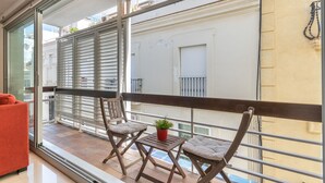 A balcony with two wooden chairs, a small table with a potted plant, and a red sofa.