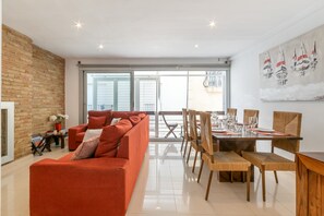 Uma sala de estar moderna com um sofá vermelho, mesa de jantar com cadeiras e uma janela grande com persianas.