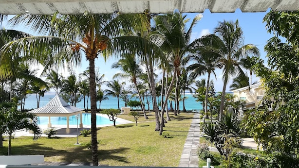 Um resort com piscina, palmeiras e vista para o oceano.