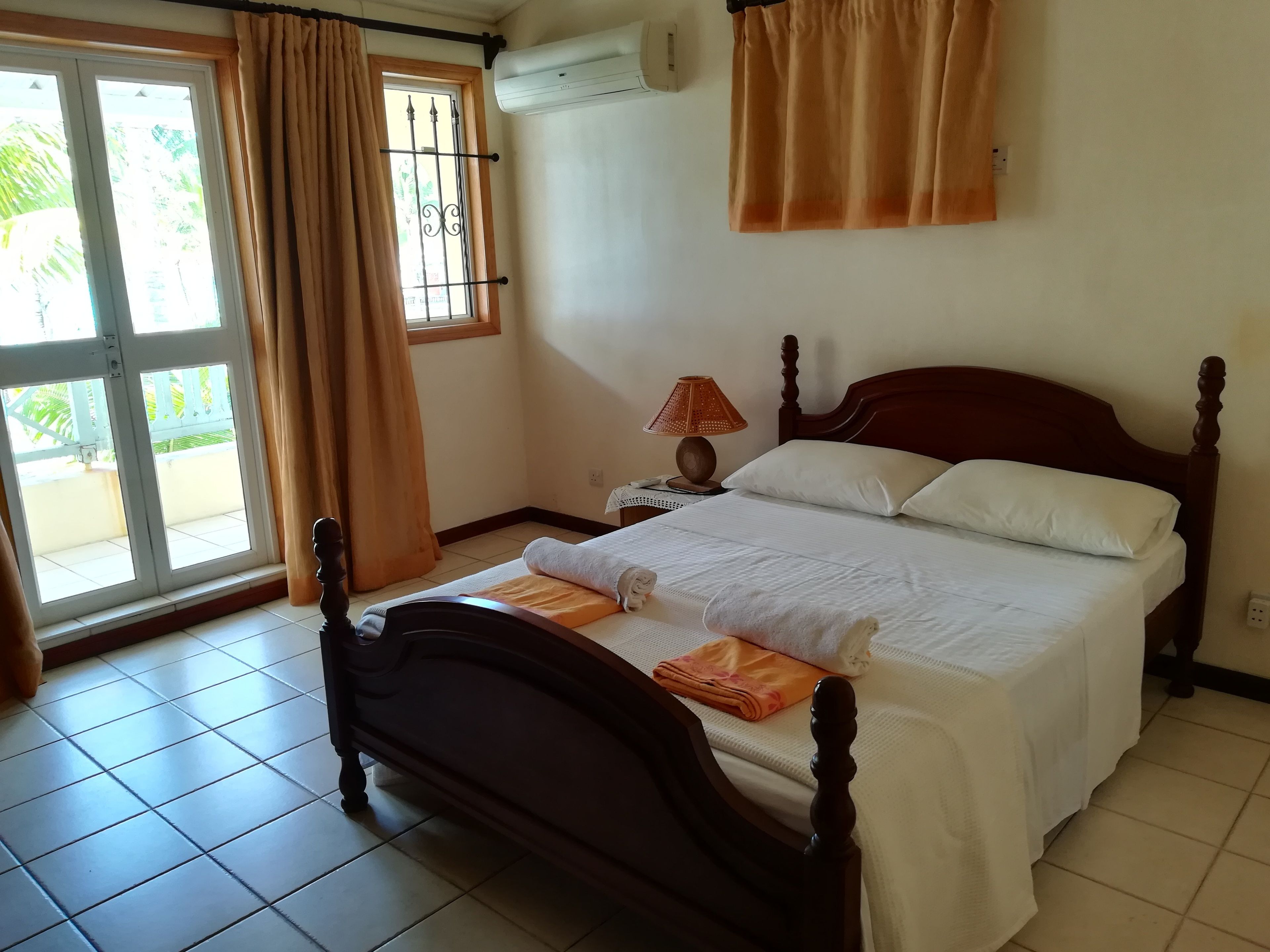 Un dormitorio con cama, cortinas, mesita de noche, lámpara y aire acondicionado.