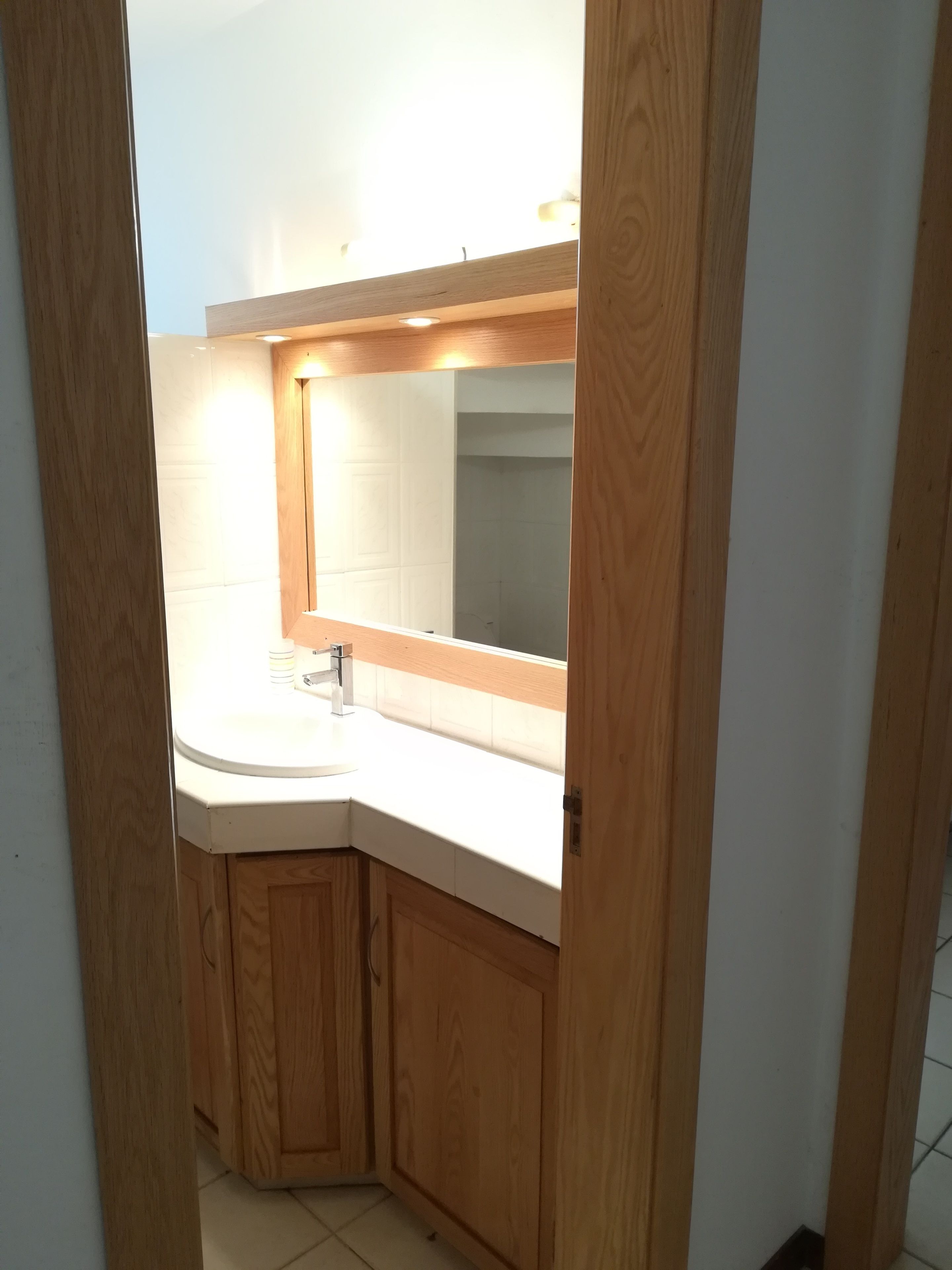 Une salle de bain avec un meuble en bois, un lavabo blanc et un miroir au-dessus.