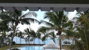Uma área de piscina com palmeiras, um gazebo e vista para o mar.