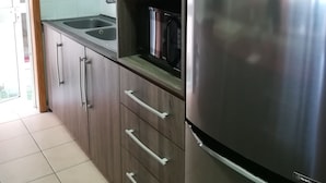 Uma cozinha com geladeira de aço inoxidável, armários de madeira, pia e micro-ondas.