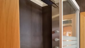 Um banheiro moderno com box de vidro, pia branca e parede revestida com azulejos escuros.