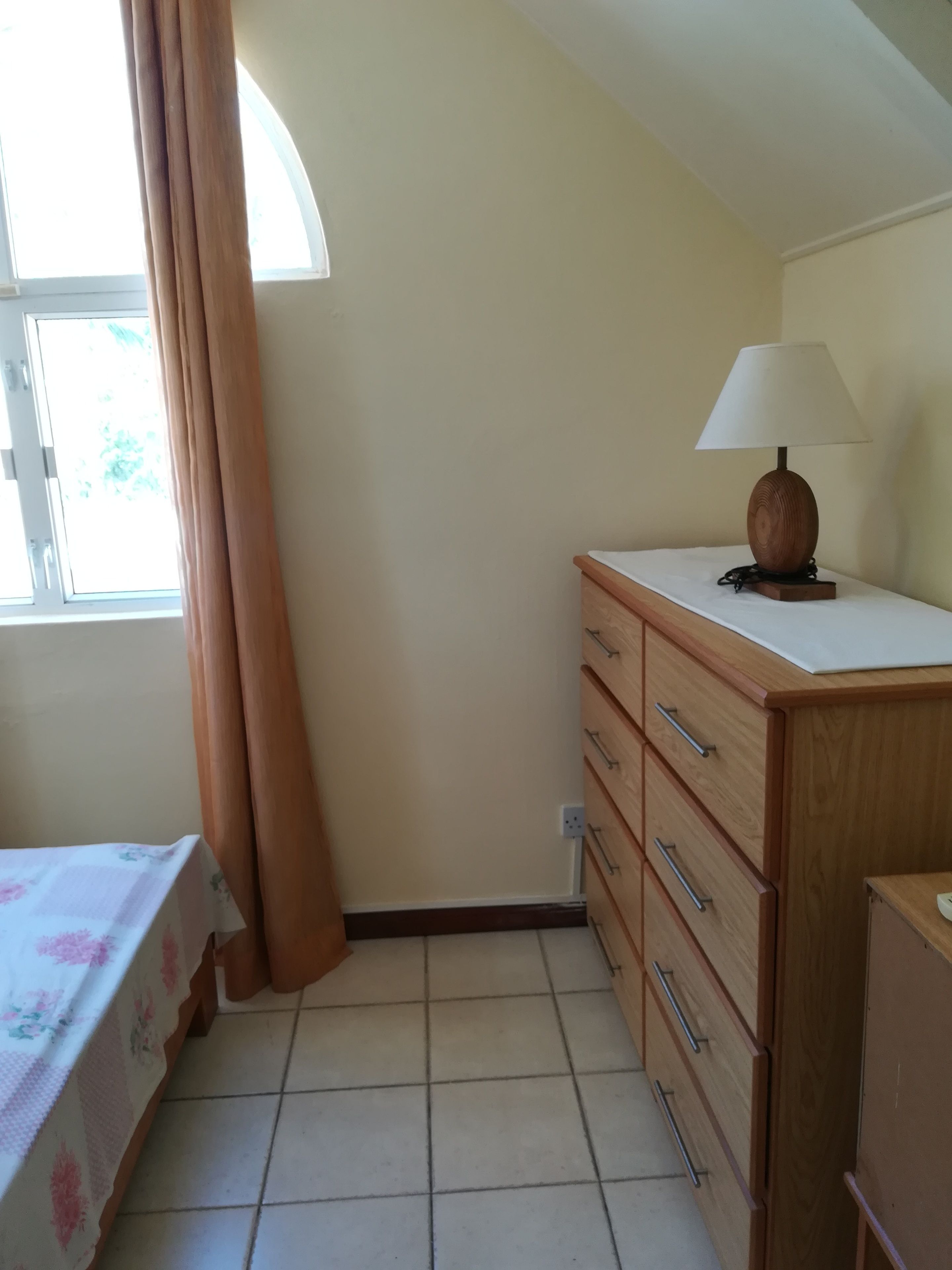 A bedroom with a bed, a dresser, a nightstand, and a lamp.