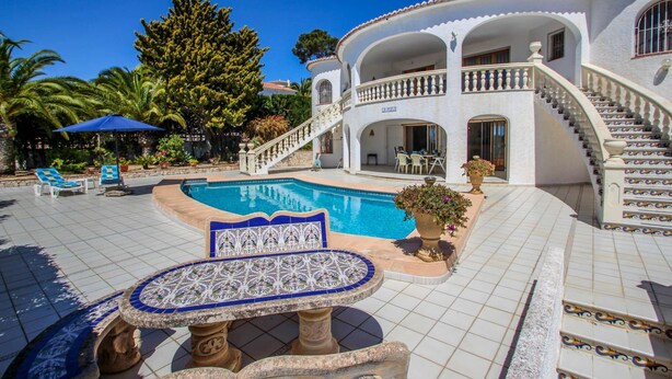A pool area with a tiled deck, a lounge chair, and a decorative table.