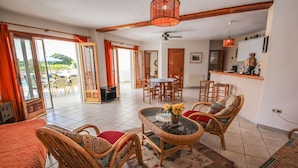 A spacious living area with wicker furniture, a glass coffee table, and a view of the outdoors.