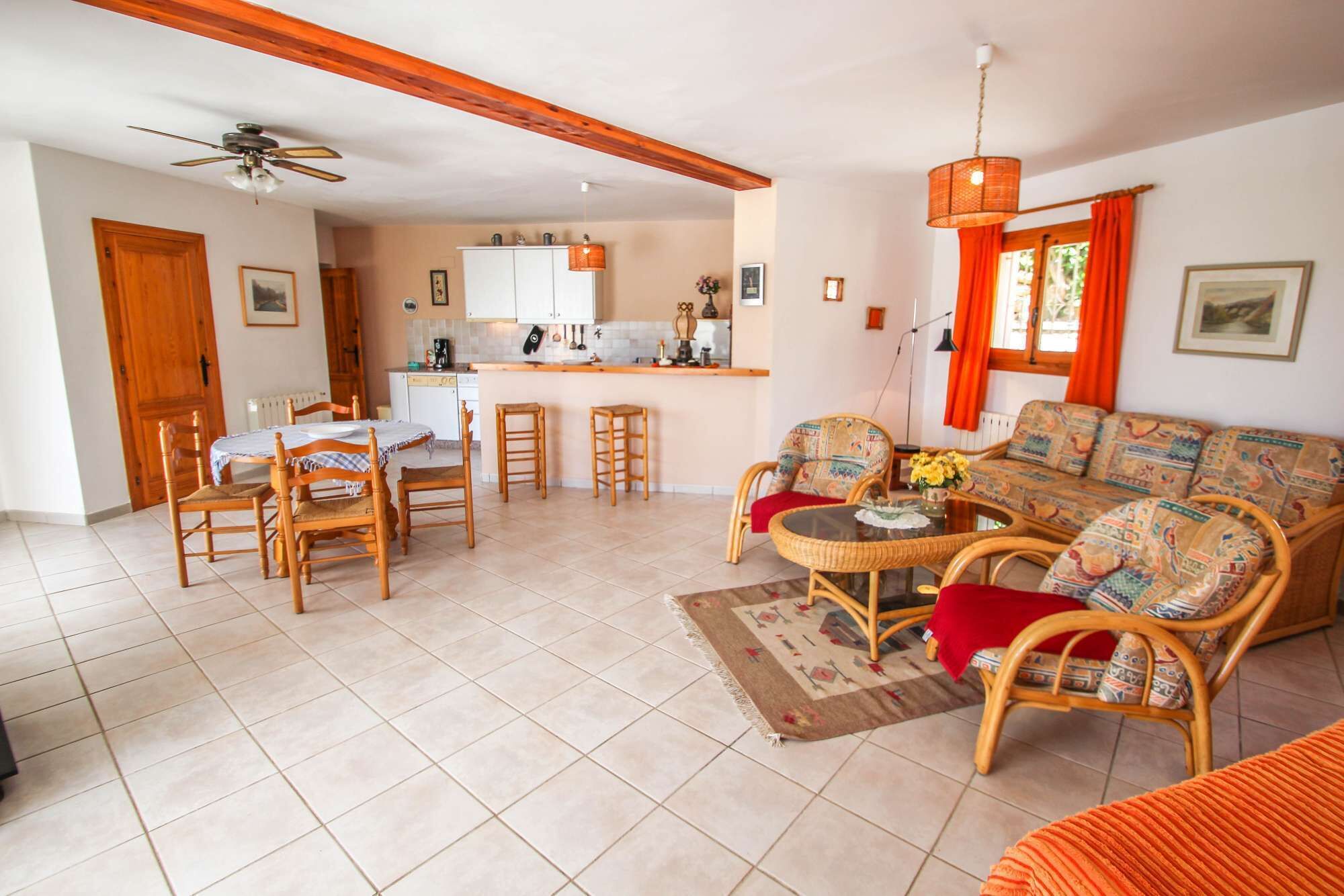 A spacious living area with a dining table, chairs, a sofa, and a kitchen in the background.