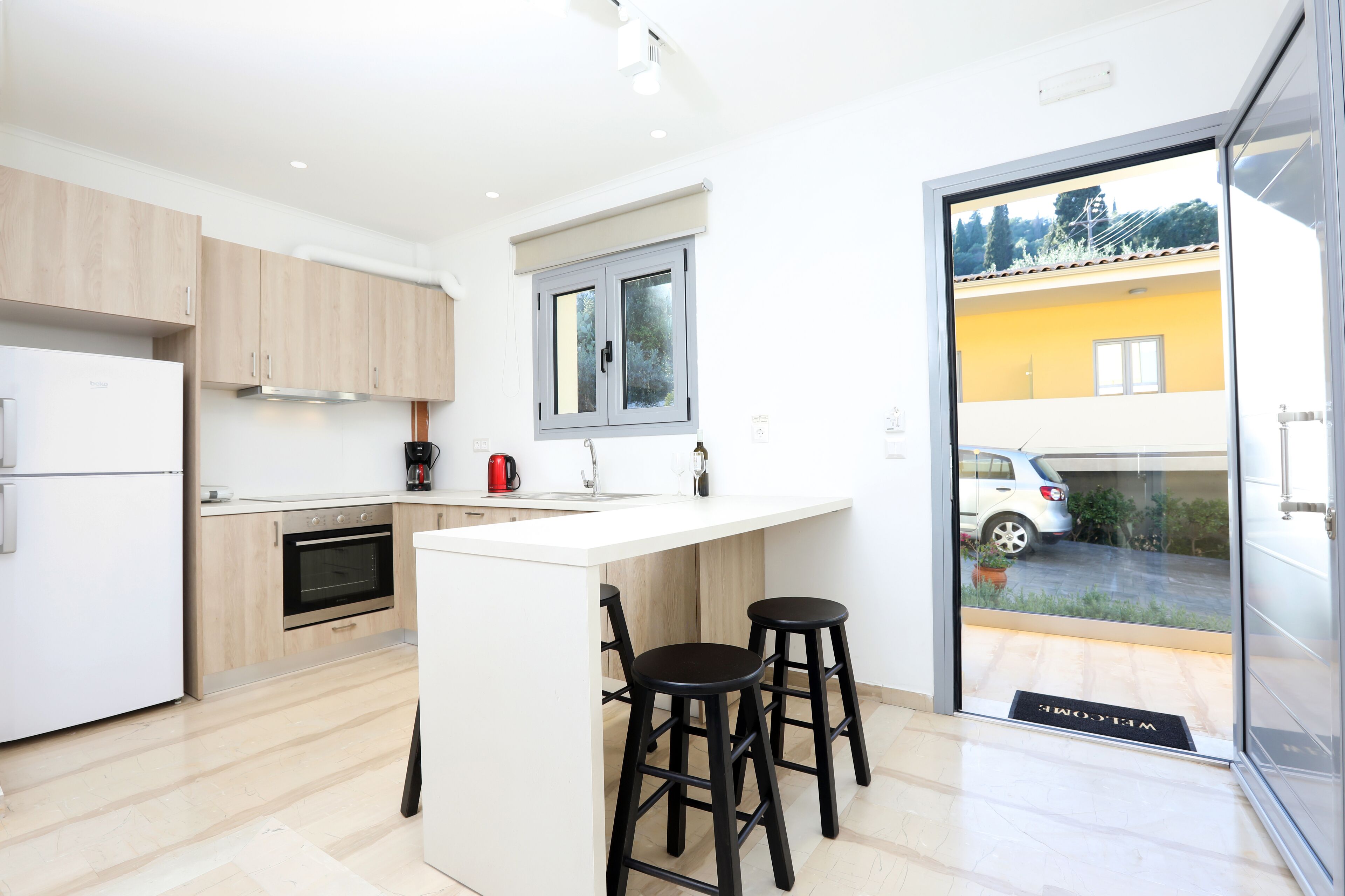 A modern kitchen with a central island, wooden cabinets, and a view through a glass door to an outdoor area.
