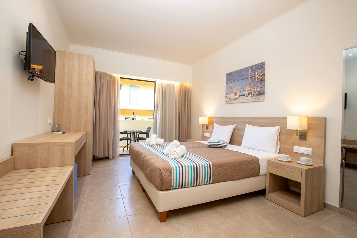 A hotel room with a bed, bedside tables, a TV, and a painting on the wall.