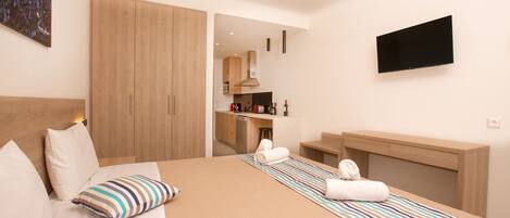 Una habitación de hotel moderna con una cama grande, un televisor de pantalla plana, un armario de madera y una kitchenette al fondo.