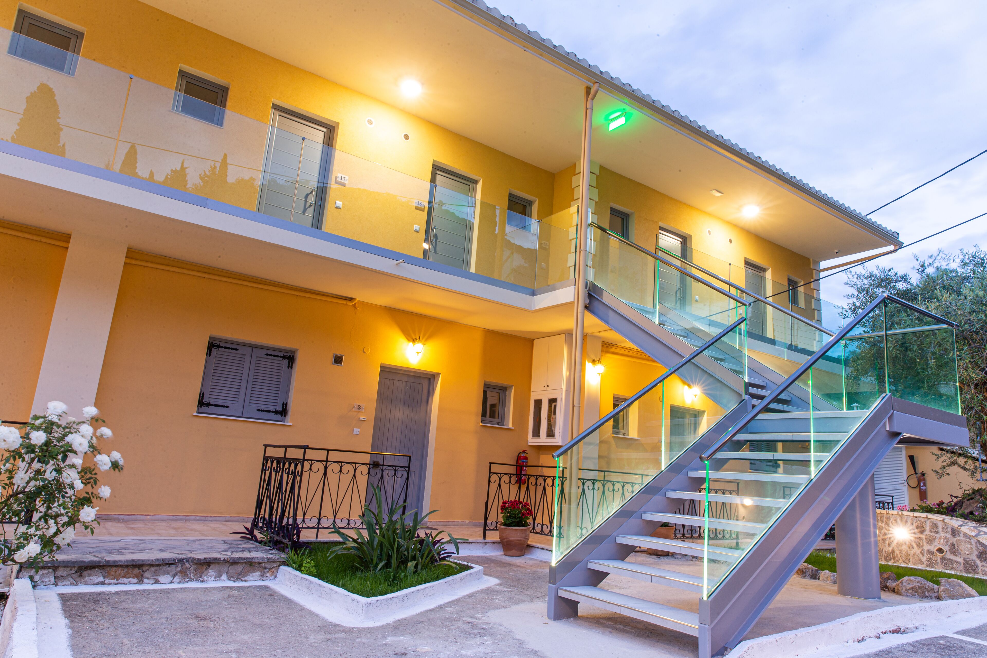 A two-story building with a glass staircase, a balcony, and a well-lit entrance.