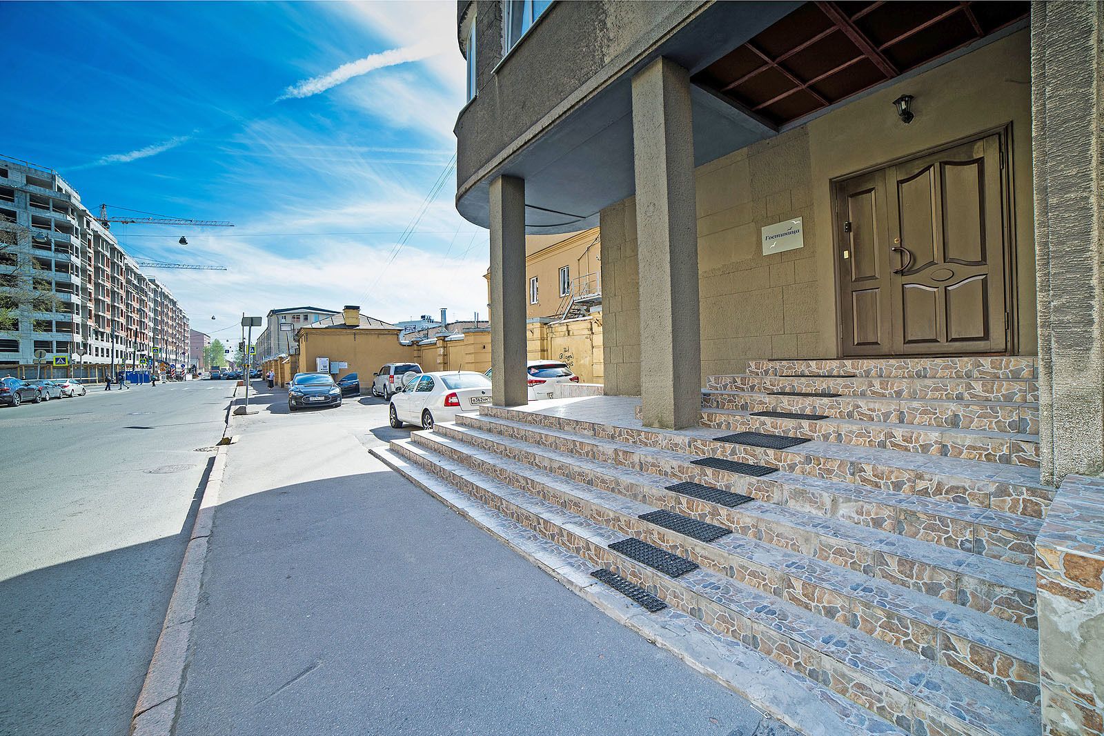 A building with stone steps leading to a door, a clear sky, and parked cars on the street.