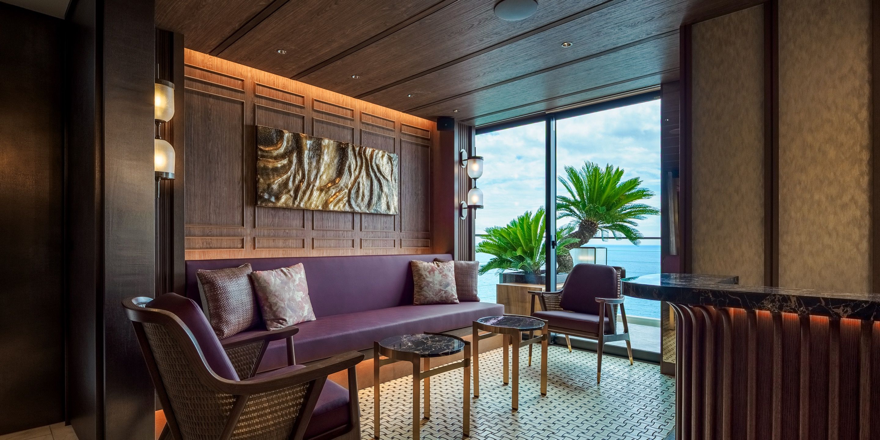 Ein moderner Lounge-Bereich mit einer Couch, Sesseln, einem kleinen Tisch und einem großen Fenster mit Blick auf den Ozean.