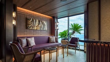 Ein moderner Lounge-Bereich mit einer Couch, Sesseln, einem kleinen Tisch und einem großen Fenster mit Blick auf den Ozean.