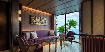 A modern lounge area with a sofa, chairs, a small table, and a large window offering a view of the ocean.